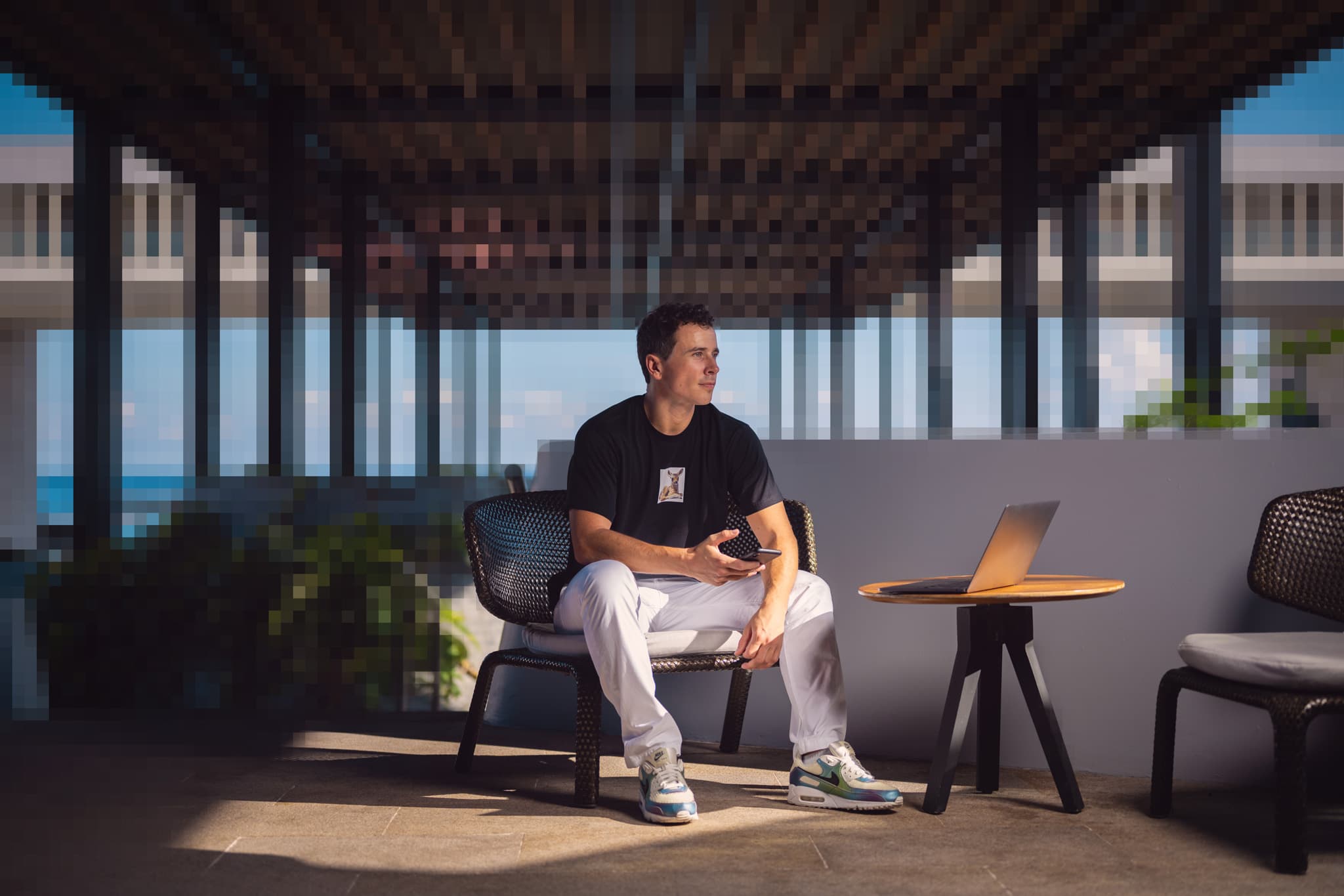 Pixelated portrait of Nicholas Oliver, seated with phone in hand, laptop beside him